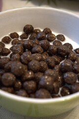 Crispy chocolate cereal balls served with milk in small bowl, nutritious breakfast for children.