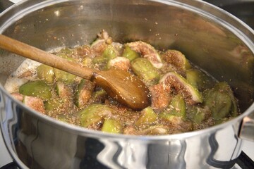 Homemade fig jam boiling in metal pot on stove, close-up preparation process.