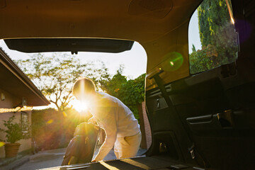 Young man putting suitcase in car trunk at sunset © mariamontoyart