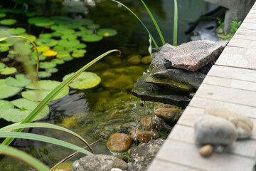 Small artificial waterfall with stones and wooden deck in a Japanese garden, symbolizing landscaping, home improvement, and traditional Japanese culture.