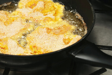 Breaded meat schnitzel frying in hot oil on pan. Golden crust forming while cooking traditional homemade cutlet. Unhealthy fast food preparation with deep frying process in kitchen.