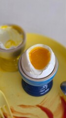 cream of egg A soft-boiled egg with a runny yolk served in a blue egg cup. The cracked shell reveals the golden yolk, placed on a yellow plate, creating a bright and appetizing breakfast scene.