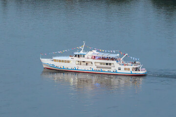 Fototapeta premium A pleasure boat sails along the River. Pleasure boat cruises along the tranquil waters of the Yenisei River showcasing scenic beauty during a summer day