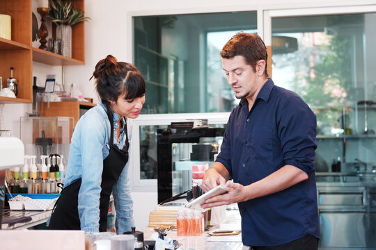 Smiling Caucasian barista woman receiving orders from customers is businessman holding tablet for to choose a menu to order drinks in cafe - Powered by Adobe
