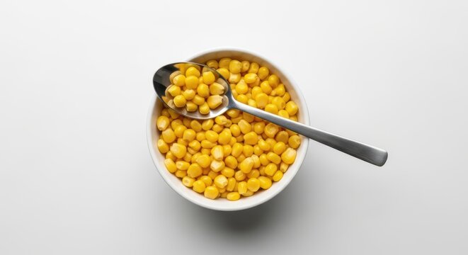 Bowl of sweet corn kernels with silver spoon on white background