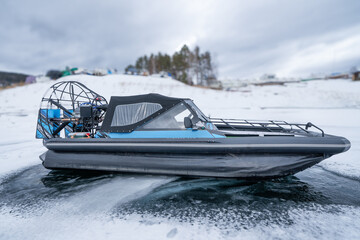 Fototapeta premium A modern hovercraft glides effortlessly over a frozen lake, showcasing its sleek design. The surrounding landscape is a serene winter scene, with snow-covered hills in the background and scattered