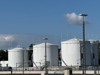 Industrial Storage Tanks Positioned Beneath a Bright Blue Sky and Fluffy White Clouds