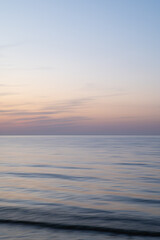 A dreamy, impressionistic paint like blurred sea sunset background with gently soft pastel colours. Vertical photo.