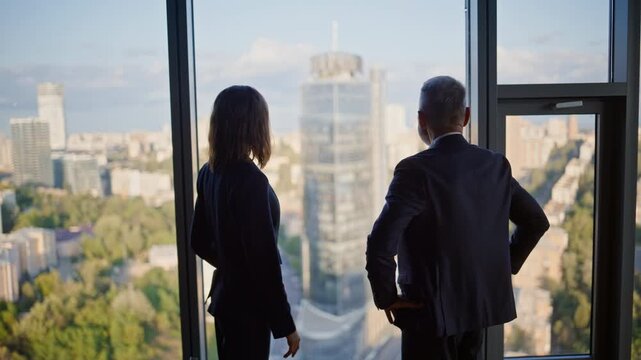 Confident partners shaking hands standing by panoramic office window together. 