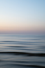 A dreamy, impressionistic paint like blurred sea sunset background with gently soft pastel colours. Vertical photo.
