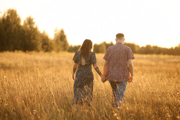 A romantic couple strolls hand-in-hand across a golden field during sunset.