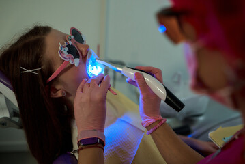 A dentist uses a curing light to treat a young patient's teeth in a dental clinic.