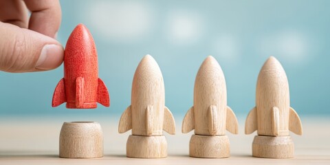 The red wooden rocket being picked up among three natural wooden rockets on desk