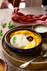 Thai mango sticky rice with coconut milk, garnished with edible flowers and mint on the table vertical photo
