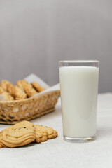 glass milk stands next to freshly baked cookies that are arranged in woven basket. setting creates warm and inviting atmosphere perfect for enjoying snack. vertical. close up.