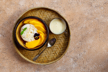 Thai mango sticky rice with coconut milk, garnished with edible flowers and mint on light background top view copy space for text
