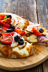 Pinsa Romana with grilled chicken breast, mozzarella cheese, tomatoes and black olives on wooden table	