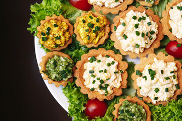 Mini tartlets with egg paste. Small appetizers with spinach filling and curry spread. Homemade finger food served on lettuce leaves and garnished with cherry tomatoes. Party buffet style snacks.