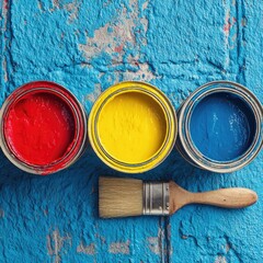 Three paint cans?red, yellow, and blue?on a textured, distressed blue surface with a paintbrush