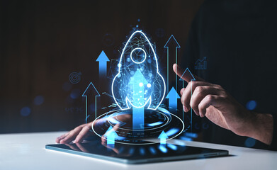 Futuristic startup launch concept with glowing rocket icon above tablet and hand gesture on dark background with blue digital arrows and HUD elements.