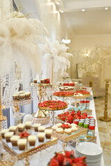 A luxurious wedding buffet in an elegant restaurant showcases a beautifully arranged sweet table with fruits, cakes, and desserts.