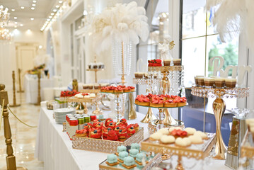 A luxurious wedding buffet in an elegant restaurant showcases a beautifully arranged sweet table with fruits, cakes, and desserts.