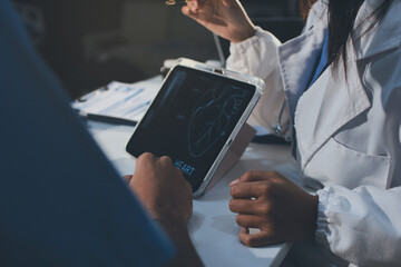 Cropped shot of an unrecognisable doctor sitting with his patient and showing her x-rays on a digital tablet