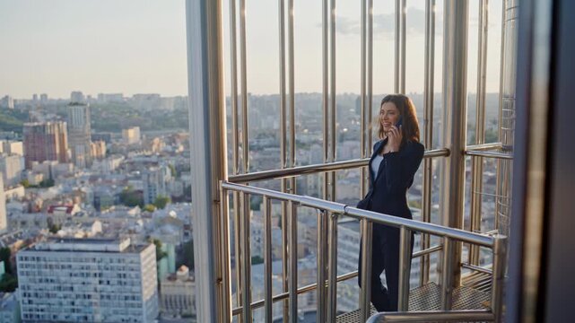 Smiling businesswoman calling balcony modern highrise building. Successful woman