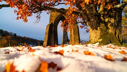 A stone archway stands beneath a magnificent oak tree, its autumn leaves ablaze against a blanket of fresh snow.