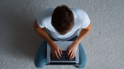Naklejka premium Young man typing on laptop sitting on carpet floor with casual clothing and focused posture in home environment