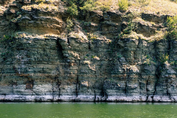 Serene riverbank with textured rocky cliffs and lush greenery reflecting in calm water, showcasing natural beauty and tranquility in a scenic landscape. Bakota bay, Dniester river, Ukraine
