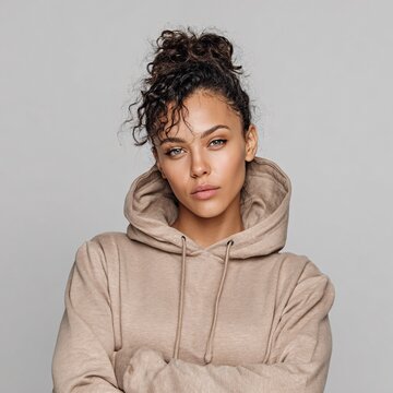 A confident woman sports a neutral taupe hoodie against a simple gray backdrop, showcasing a stylish and relaxed aesthetic.