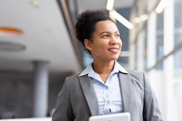 Confident business professional working on tablet, looking forward with optimistic vision in modern, sunlit corporate workspace