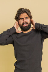 Fototapeta premium Dont want to hear and listen. Frustrated annoyed irritated Lebanese man covering ears gesturing No, avoiding advice ignoring unpleasant noise loud voices. Indian Hispanic guy alone on beige background