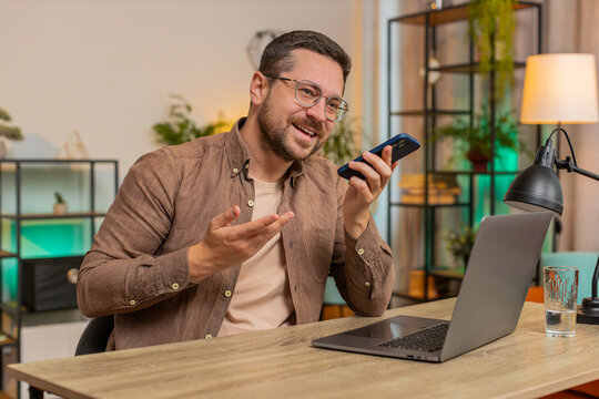 Caucasian young businessman working, having mobile phone loudspeaker talk at office desk with laptop. Manager freelance man guy holding smartphone using messenger chat apps. Employment, occupation.