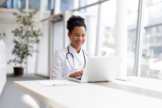 Smiling female doctor working on a laptop in a modern clinic, blending healthcare with technology in a bright, inviting environment