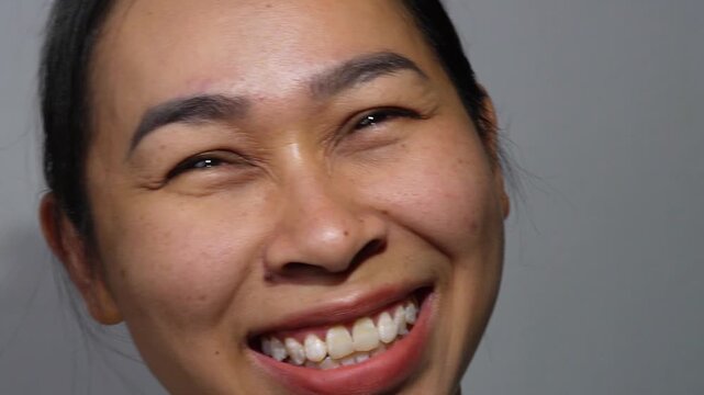 A close-up portrait of an Asian woman smiling happily, showing teeth and facial wrinkles around the eyes.