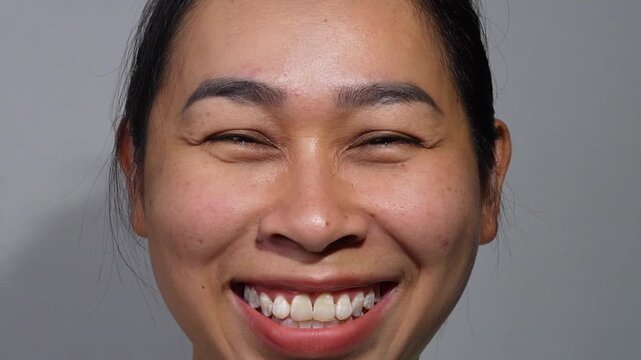 A close-up portrait of an Asian woman smiling happily, showing teeth and facial wrinkles around the eyes.