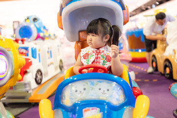 A cute little Asian girl is riding a toy car in an amusement park,Asian Chinese little girl driving...
