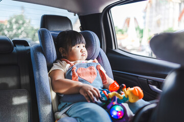 A cute little Asian girl is sitting playing with a toy in a car seat during a car trip,Asian child girl is playing her toy in the car while traveling to school. Childhood and family lifestyles in car 
