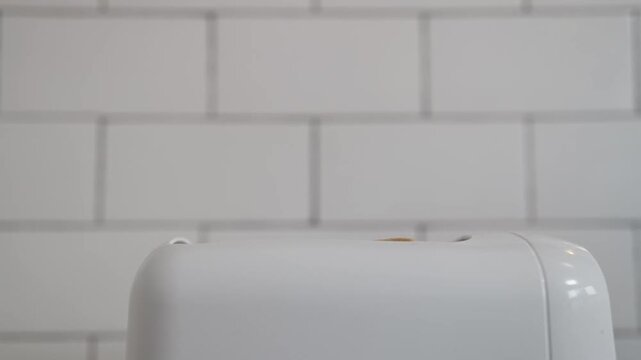 White electric toaster toasting bread in front of a white tile background