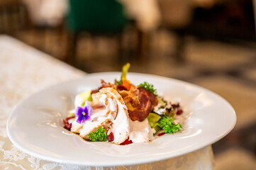Gourmet dish with roasted poultry, crispy bacon, creamy sauce, and edible flower garnish, elegantly plated in a fine dining setting