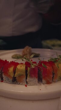cinematic 4k vertical video chef plating rainbow sushi rolls with arugula garnish in asian restaurant