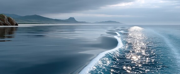 Calm ocean waters reflecting a cloudy sky with distant mountains