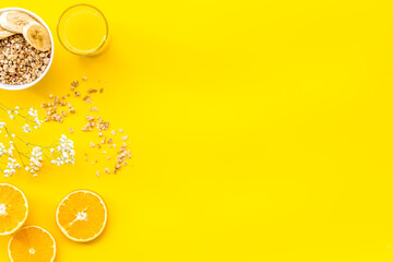 granola with banana slices and orange juice for breakfast on yellow background top view copyspace