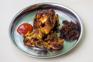 Delicious whole fried country chicken served on a steel plate with a side of tomato sauce. A tasty, spicy, and smoky homemade barbecue meal perfect for dinner.