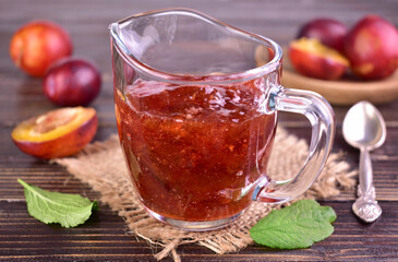Pink plum jam in a glass sauceboat on a dark wooden background. Close-up.
