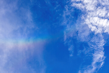 Gorgeous blue sky background filled with beautiful white cumulus clouds and a subtle, delicate rainbow. The perfect backdrop for a tranquil and clear day.