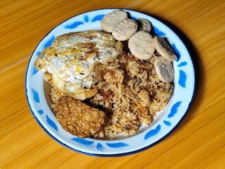 Authentic Indonesian fried rice with sunny side up egg, crackers and fried tempeh on a classic enamel plate.
