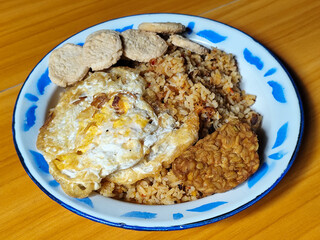 Authentic Indonesian fried rice with sunny side up egg, crackers and fried tempeh on a classic enamel plate.